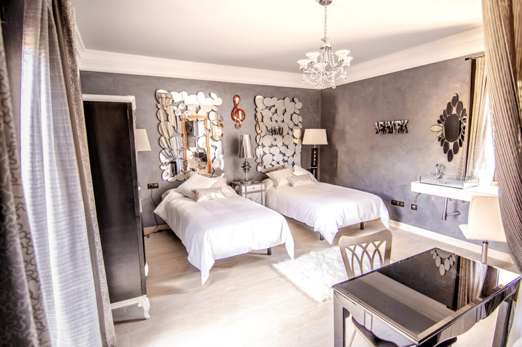 Room USA with two single beds with two mirrors on the headboards. Chandelier and walls in gray.