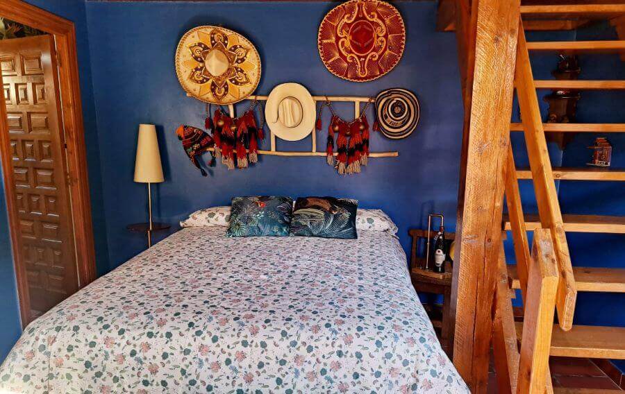 Casa del Trotamundos Hispanoamérica room with double bed and headboard with blue background and Hispanic hats
