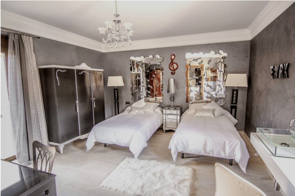 Habitación USA con dos camas individuales con dos espejos sobre los cabeceros. Lampara de araña y paredes en gris con armario de tres puertas en gris oscuro