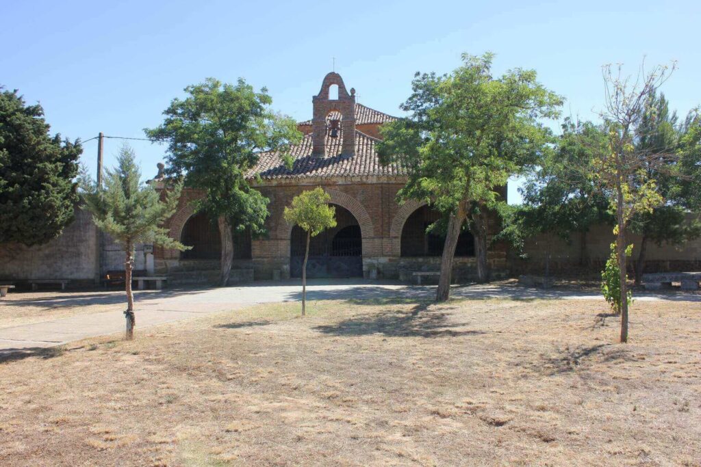 Ermita de Villafrechos con arboles delante de la entrada de arcos.